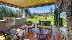 A covered outdoor patio with a grill, seating area, and a stone wall with a television. - Spacious Carnation Home w/ Grill & Large Yard (Carnation)