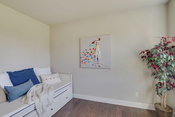 A bedroom with a bed, pillows, a blanket, a wall-mounted painting, and a potted plant.