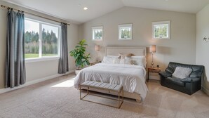 A spacious bedroom with a large bed, a bench, a black leather chair, and a potted plant. - Spacious Carnation Home w/ Grill & Large Yard (Carnation)