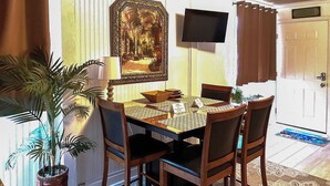 Un espace repas comprenant une table, des chaises, une plante en pot, un téléviseur et une porte.