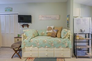 Un dormitorio con una cama, televisión, armario y estante con libros y una botella.