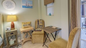 Une chambre décorée sur le thème de la plage, avec un petit bureau, une chaise et une lampe. On y trouve également des coussins décoratifs et une horloge murale.