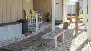 Un espace extérieur abrité, aménagé avec un banc, des chaises et une poubelle.