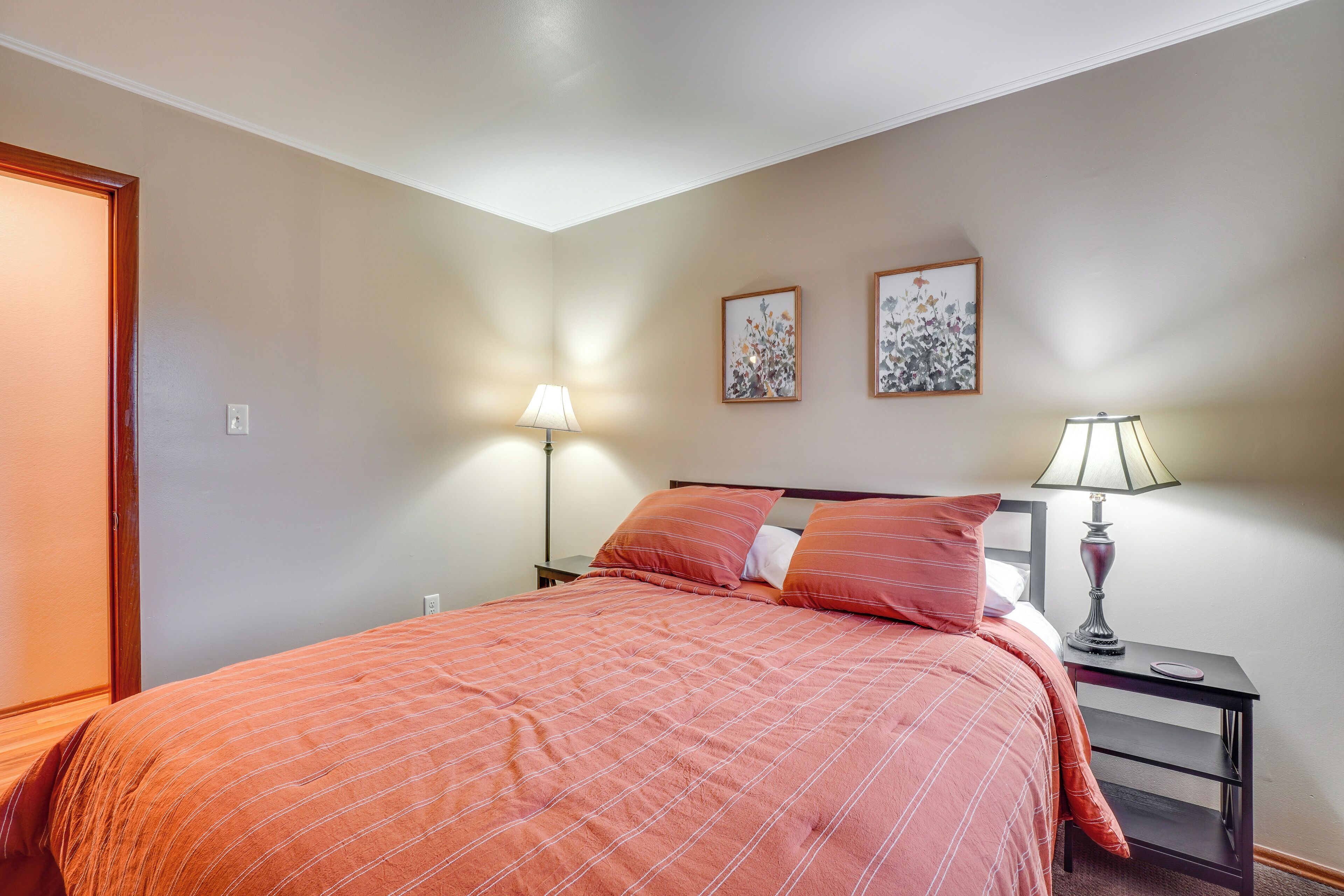 A neatly made bed with a checkered bedspread, two bedside lamps, and two framed floral artworks on the wall.