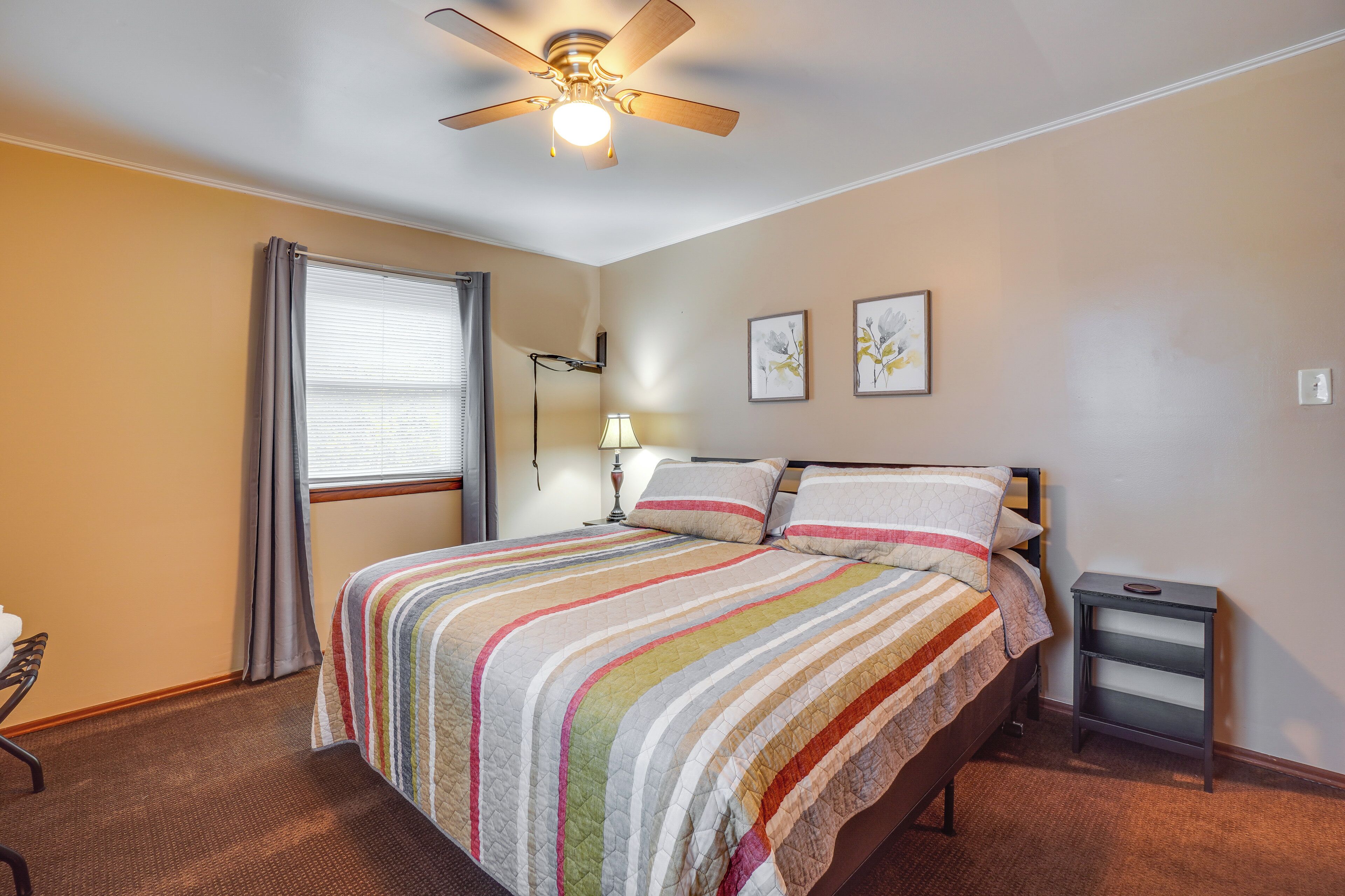 A bedroom with a bed, a ceiling fan, a bedside table, and a window with curtains.