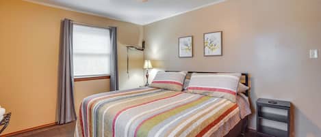 A bedroom with a bed, a ceiling fan, a bedside table, and a window with curtains.