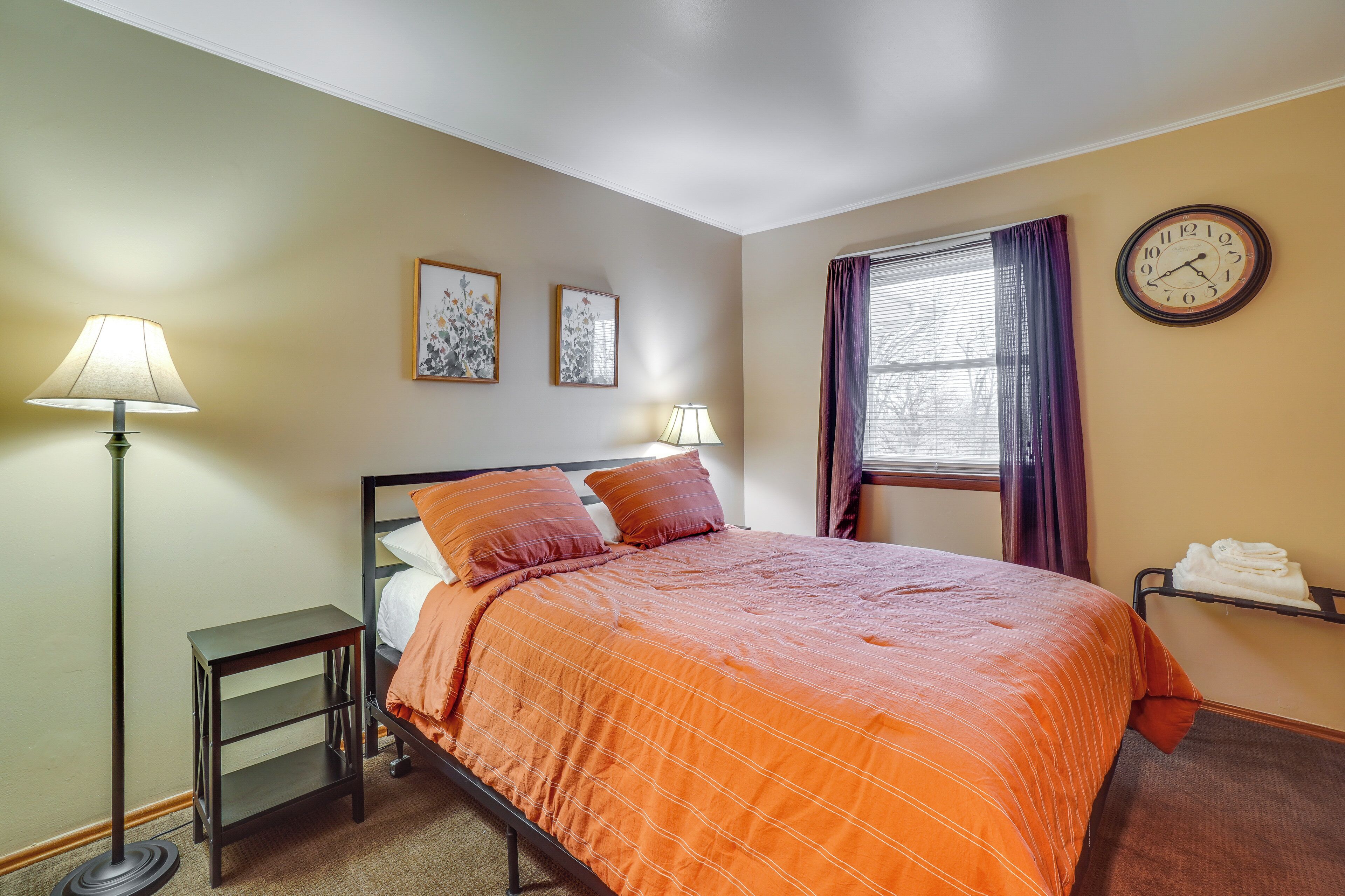 Un lit bien fait, avec une couverture orange, une lampe de chevet et une horloge murale.