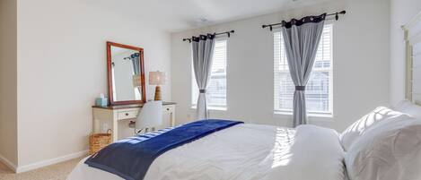 Une chambre à coucher comprenant un lit, une commode, un miroir et deux fenêtres avec des rideaux.