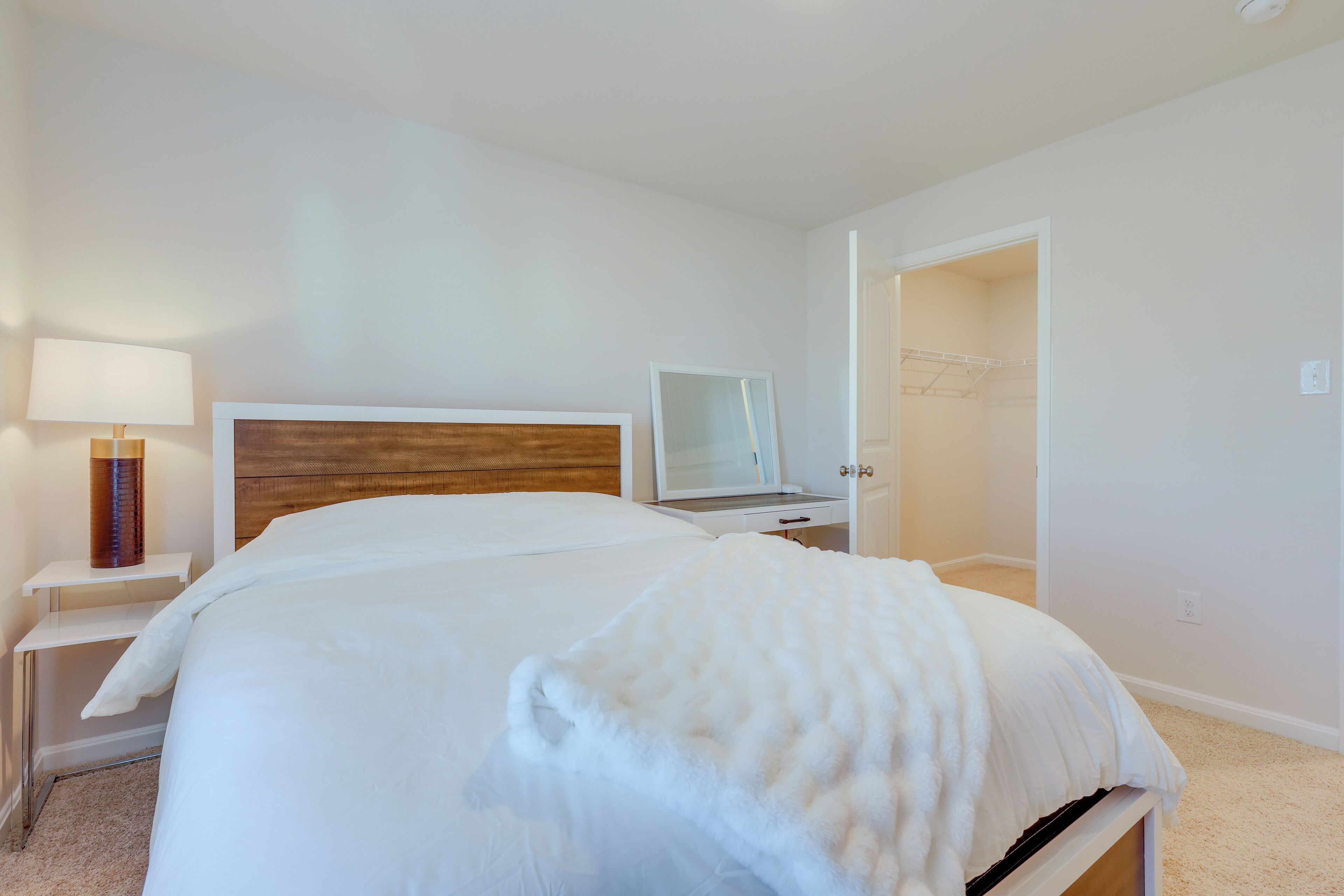 Une chambre d’hôtel avec un grand lit, une table de chevet avec une lampe, un miroir et un dressing.