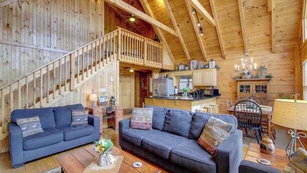 A spacious living area with a wooden staircase, a kitchen, and a dining area. - Smoky Mountains Cabin w/ Hot Tub, Deck & Views! (Sevierville)