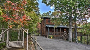 A rustic cabin with a porch and a swing set in a wooded area. - Smoky Mountains Cabin w/ Hot Tub, Deck & Views! (Sevierville)