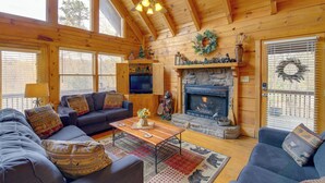 A cozy cabin interior with a fireplace, wooden walls, and a ceiling fan.