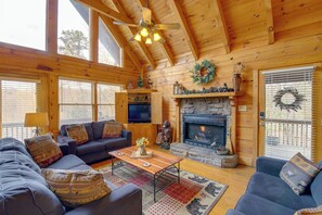 A cozy cabin interior with a fireplace, wooden walls, and a ceiling fan. - Smoky Mountains Cabin w/ Hot Tub, Deck & Views! (Sevierville)