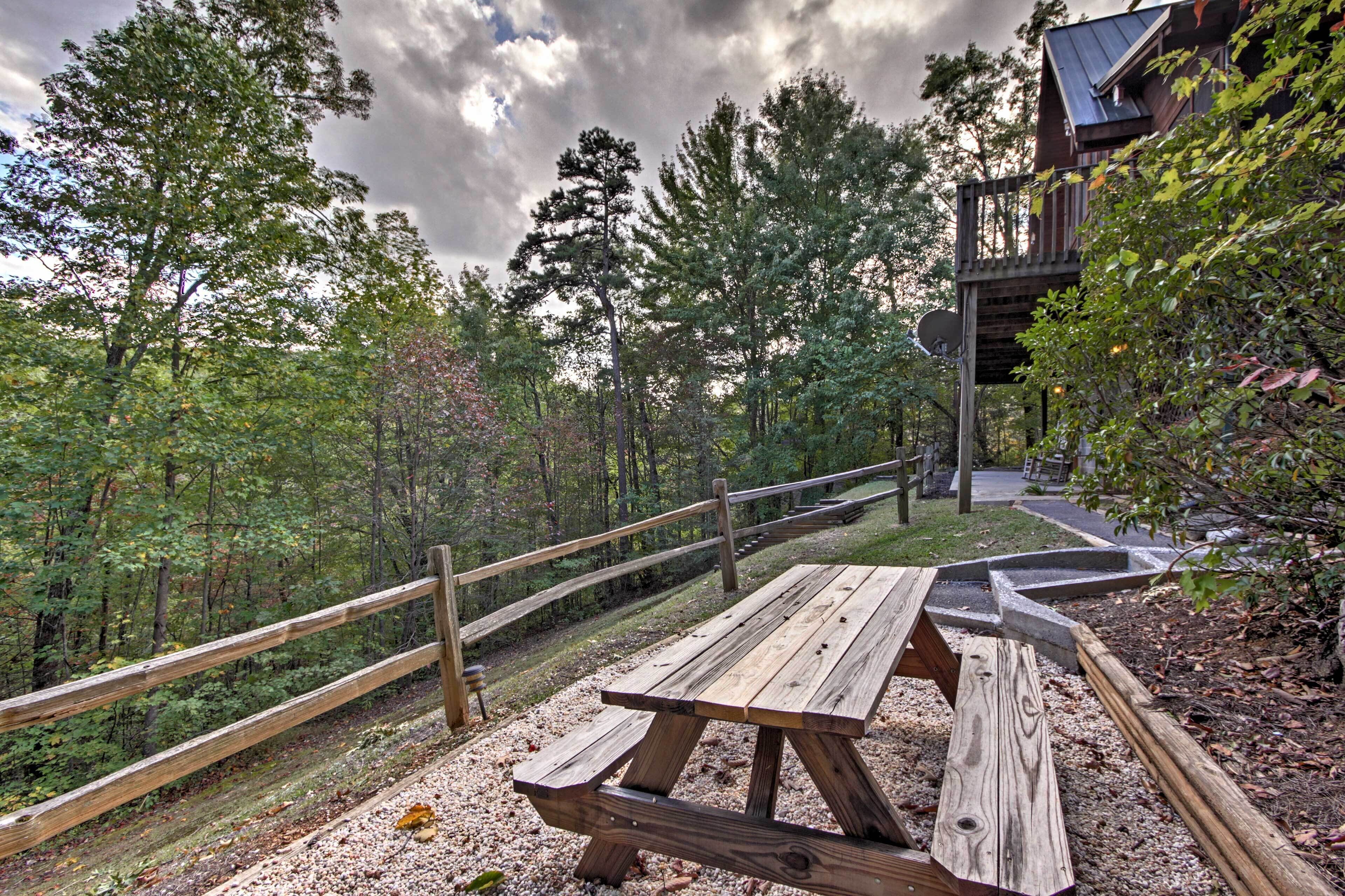 A wooden picnic table in a forested area with a wooden fence and a building with a balcony.