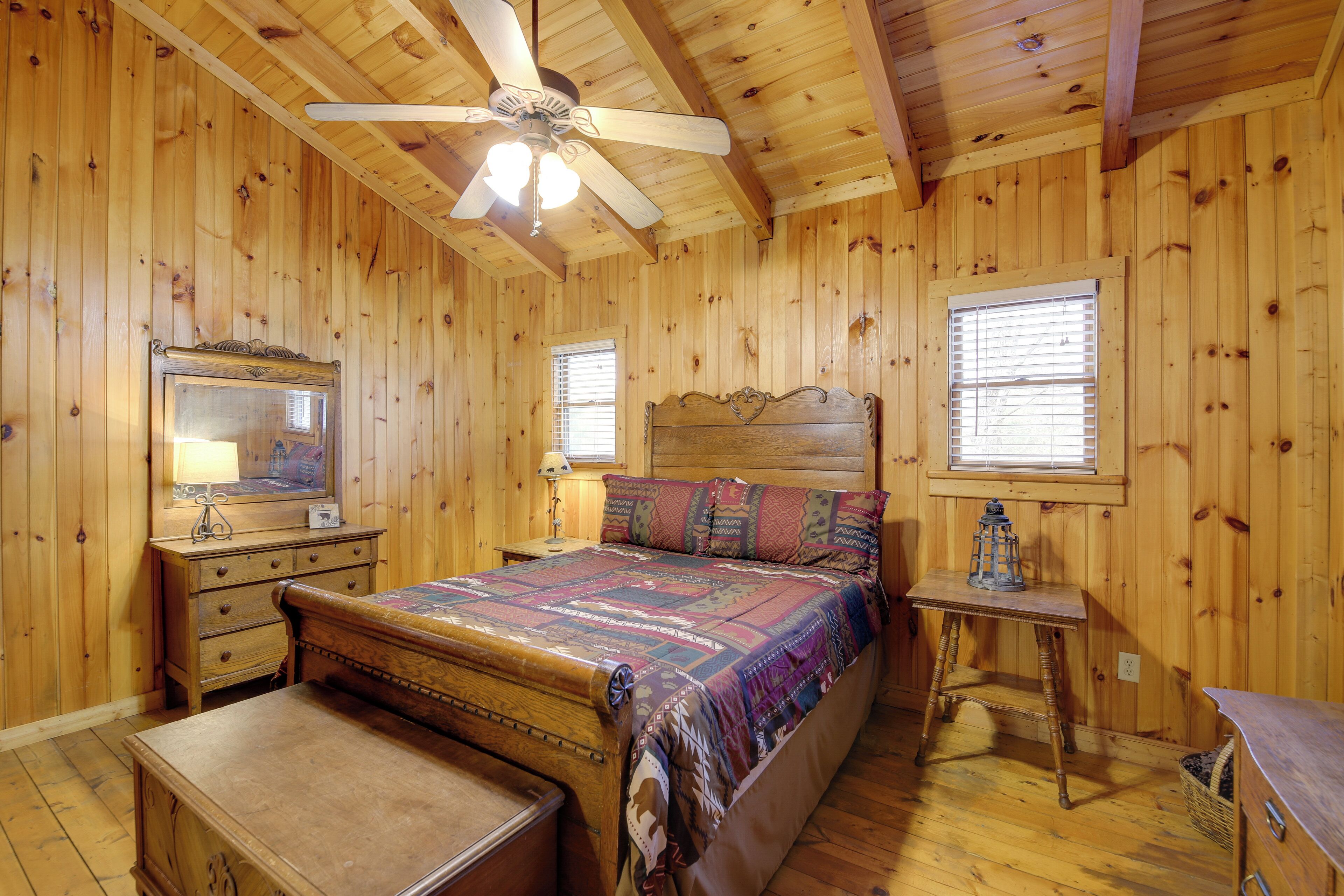 A wooden-paneled bedroom with a bed, dresser, nightstand, and a ceiling fan.