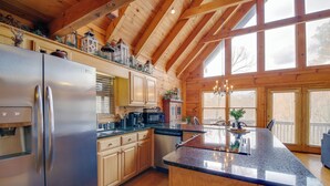 A kitchen with wooden cabinets, a stainless steel refrigerator, a granite countertop, and a large window.