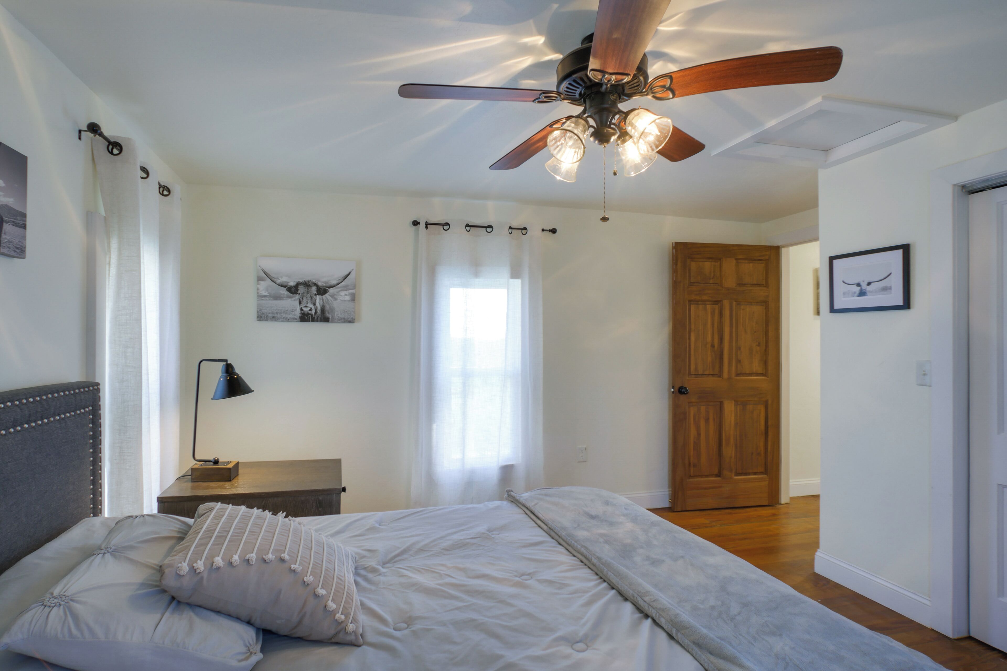 A bedroom with a bed, a ceiling fan, a nightstand, a lamp, and a door.