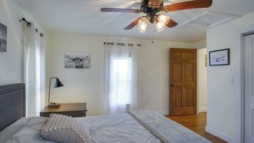 A bedroom with a bed, a ceiling fan, a nightstand, a lamp, and a door.