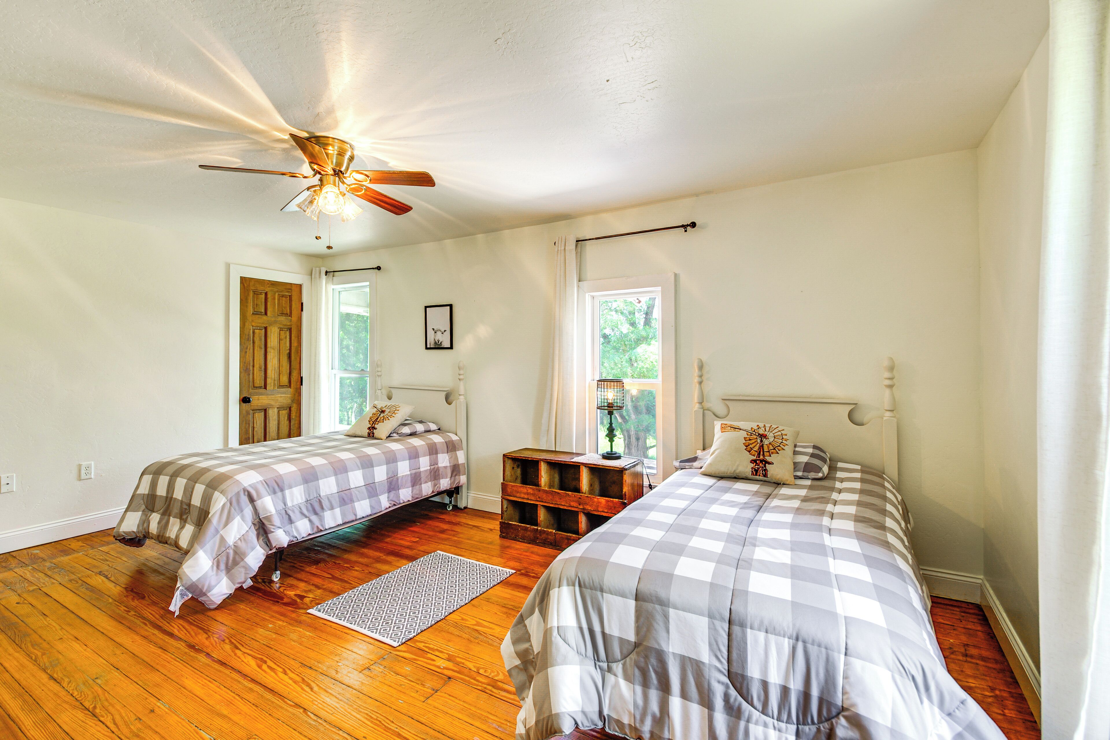 A bedroom with two beds, wooden flooring, a ceiling fan, and a window with curtains.