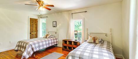 A bedroom with two beds, wooden flooring, a ceiling fan, and a window with curtains.