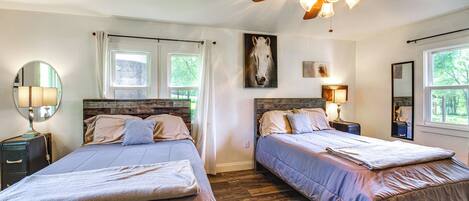 Ein Schlafzimmer mit zwei Betten, Holzboden, Deckenventilator und großen Fenstern.