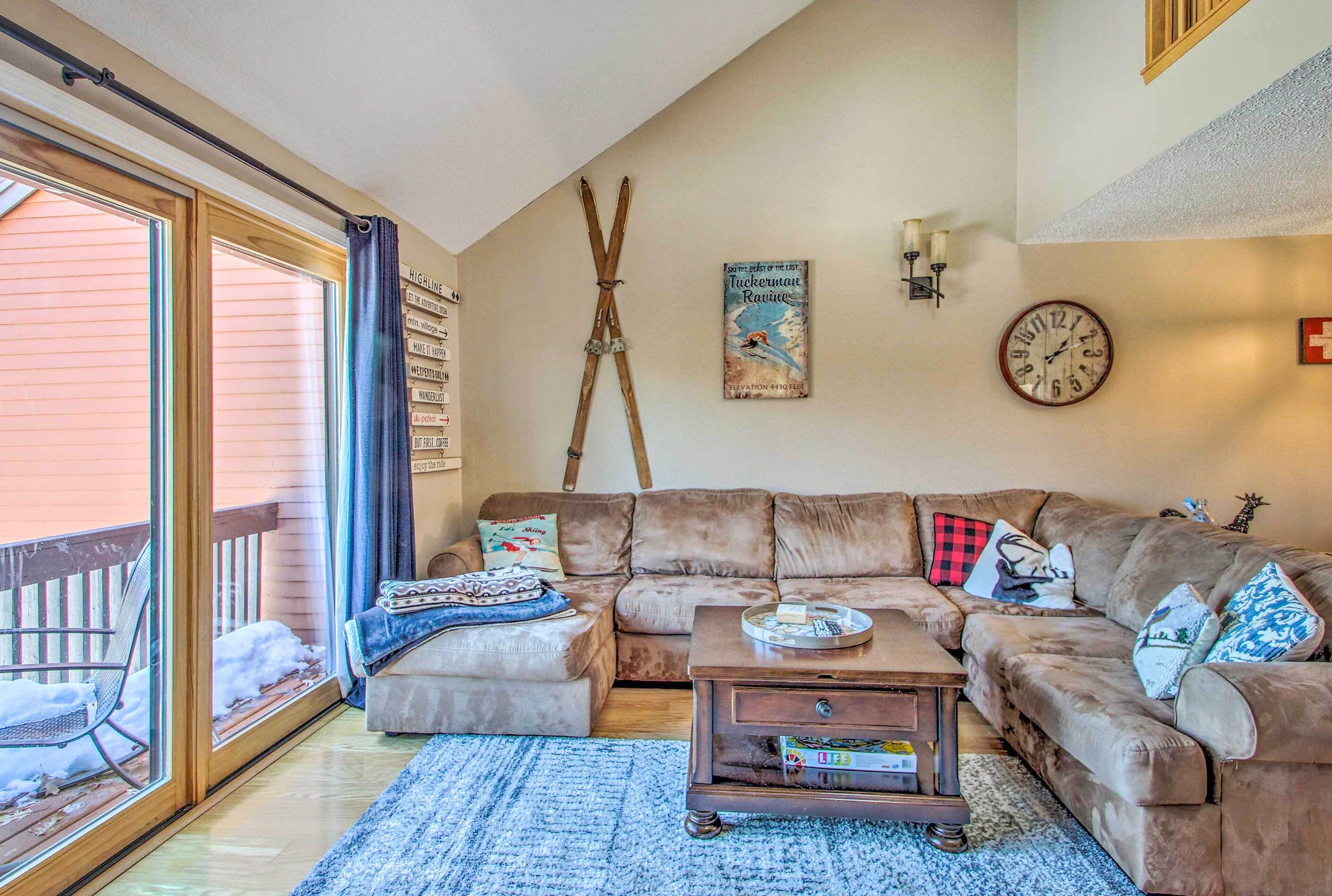 A cozy living room with a large sectional sofa, a coffee table, and a sliding glass door leading to a balcony.