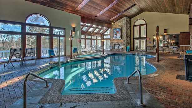An indoor swimming pool with a wooden ceiling, lounge chairs, and a stone wall. - Ski Condo w/ Pool, Close to Story Land & Attitash! (Glen)