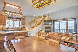 Una cocina amplia con una isla central, una mesa de comedor de madera y asientos integrados. Una escalera en espiral conduce a una zona de altillo con chimenea.