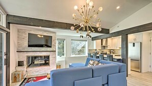 A modern living room with a large blue sectional sofa, a fireplace, and a kitchen in the background. - Snowmass Condo: Great Proximity to Chair Lift (Snowmass Village)