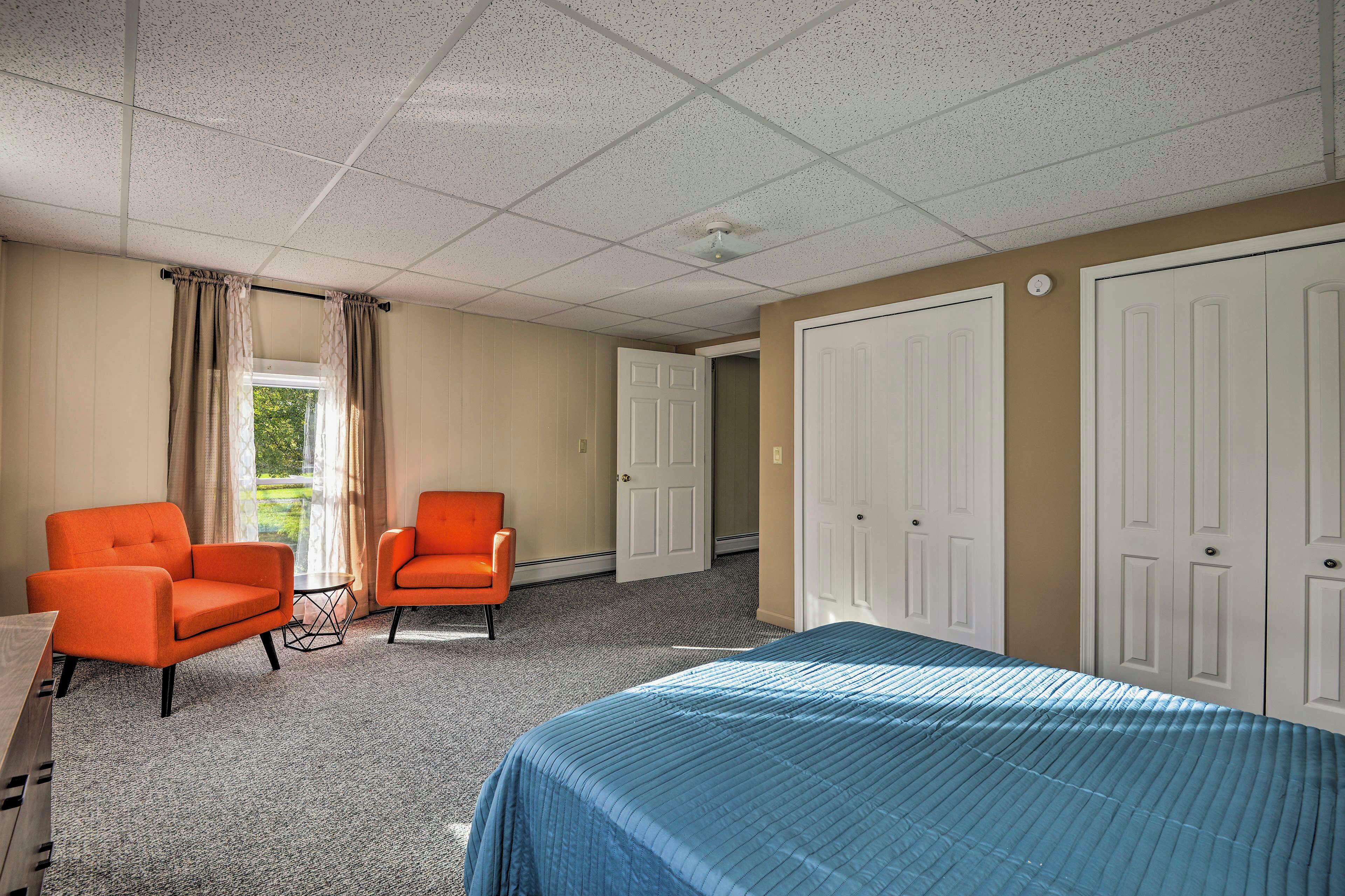 Een hotelkamer met twee oranje fauteuils, een bed met een blauw sprei, een raam met gordijnen en een deur.