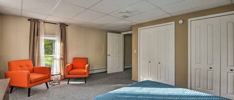 Een hotelkamer met twee oranje fauteuils, een bed met een blauw sprei, een raam met gordijnen en een deur.
