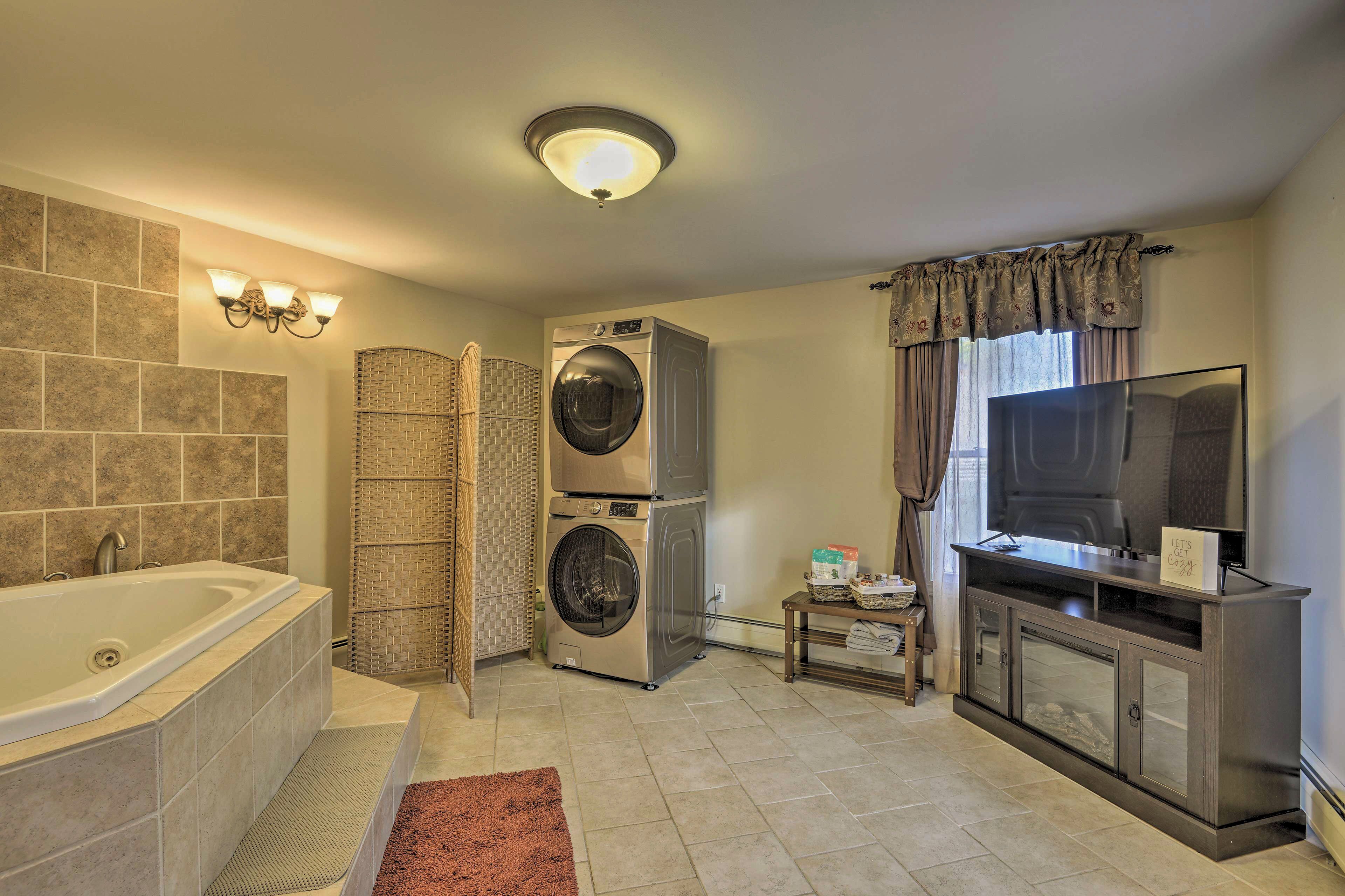 A bathroom with a bathtub, stacked washer and dryer, and a vanity with a mirror and television.