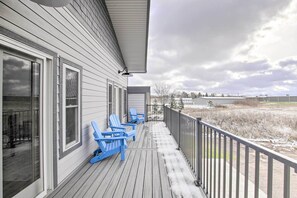 A covered porch with blue Adirondack chairs, a railing, and a view of a field. - Spacious Recently Built Home < 1 Mi to Lake! (Malone)