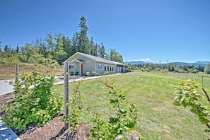 A single-story house with a porch, surrounded by a fenced yard and a forested area. - Sequim Cottage w/ Panoramic Olympic Mtn. Views! (Sequim)