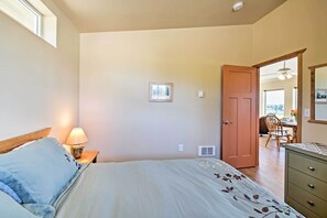 A bedroom with a bed, a nightstand with a lamp, a wooden door, and a view of a dining area. - Sequim Cottage w/ Panoramic Olympic Mtn. Views! (Sequim)