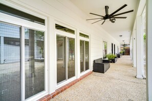 Un espacio al aire libre techado con ventilador de techo, ventanas amplias y mobiliario exterior.