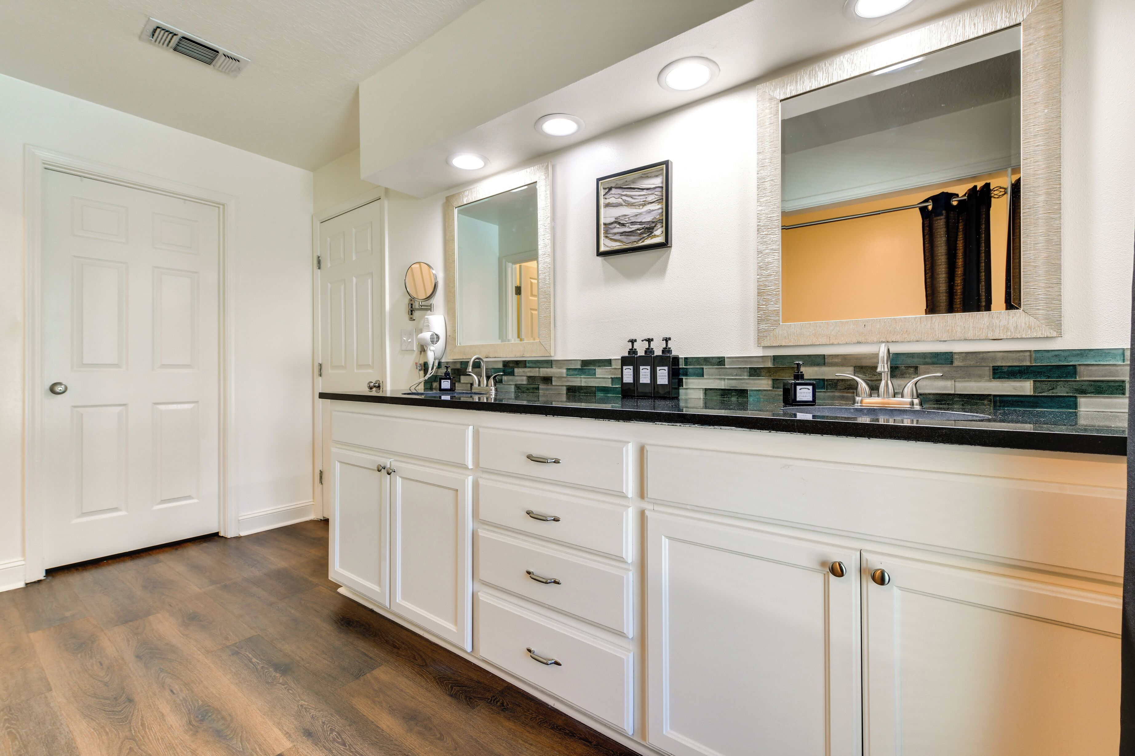 A modern bathroom with white cabinetry, a glass backsplash, and a large mirror.