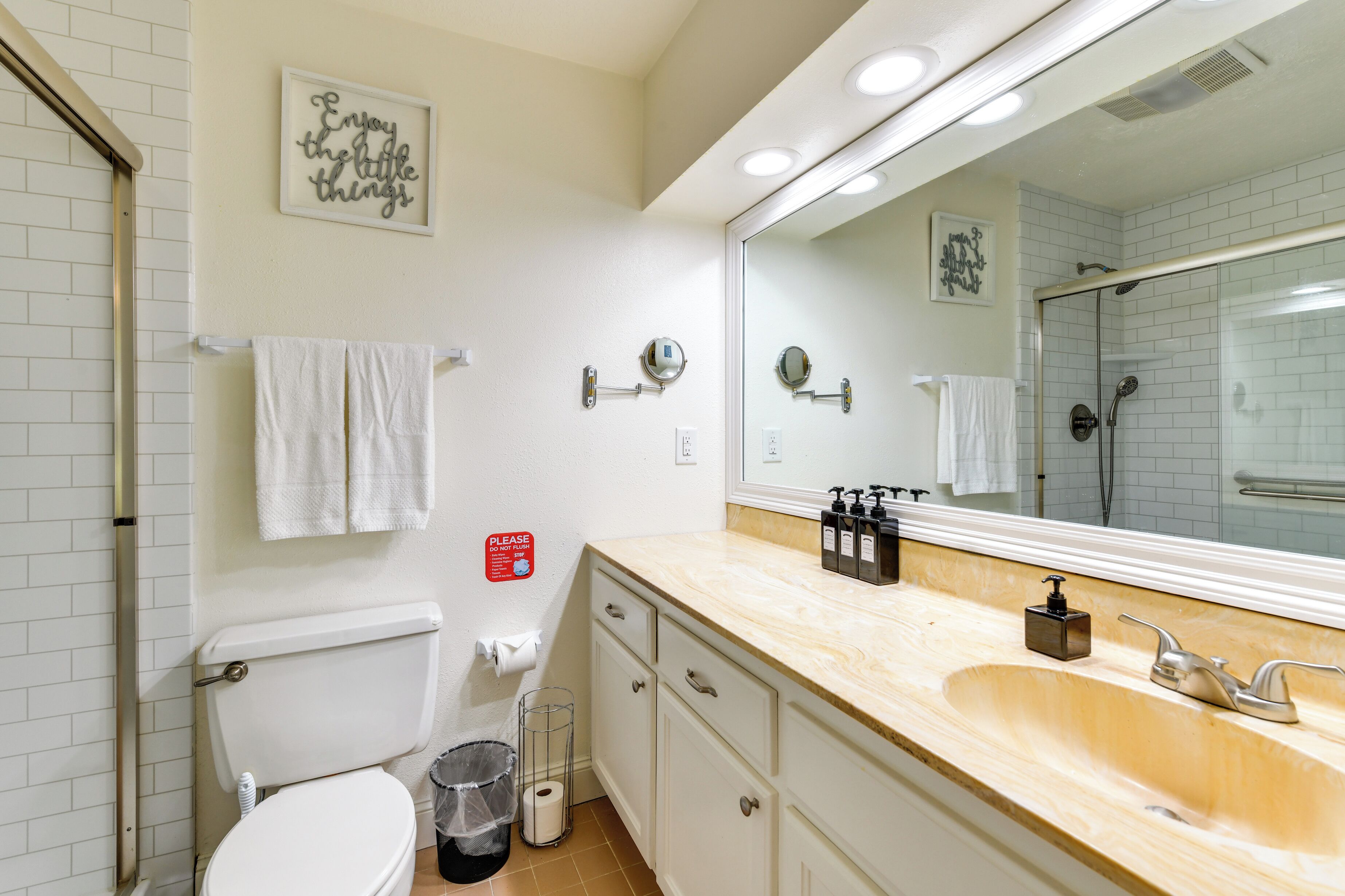A bathroom with a toilet, sink, and mirror. There are towels hanging on the wall and a sign with a message.