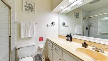 A bathroom with a toilet, sink, and mirror. There are towels hanging on the wall and a sign with a message.