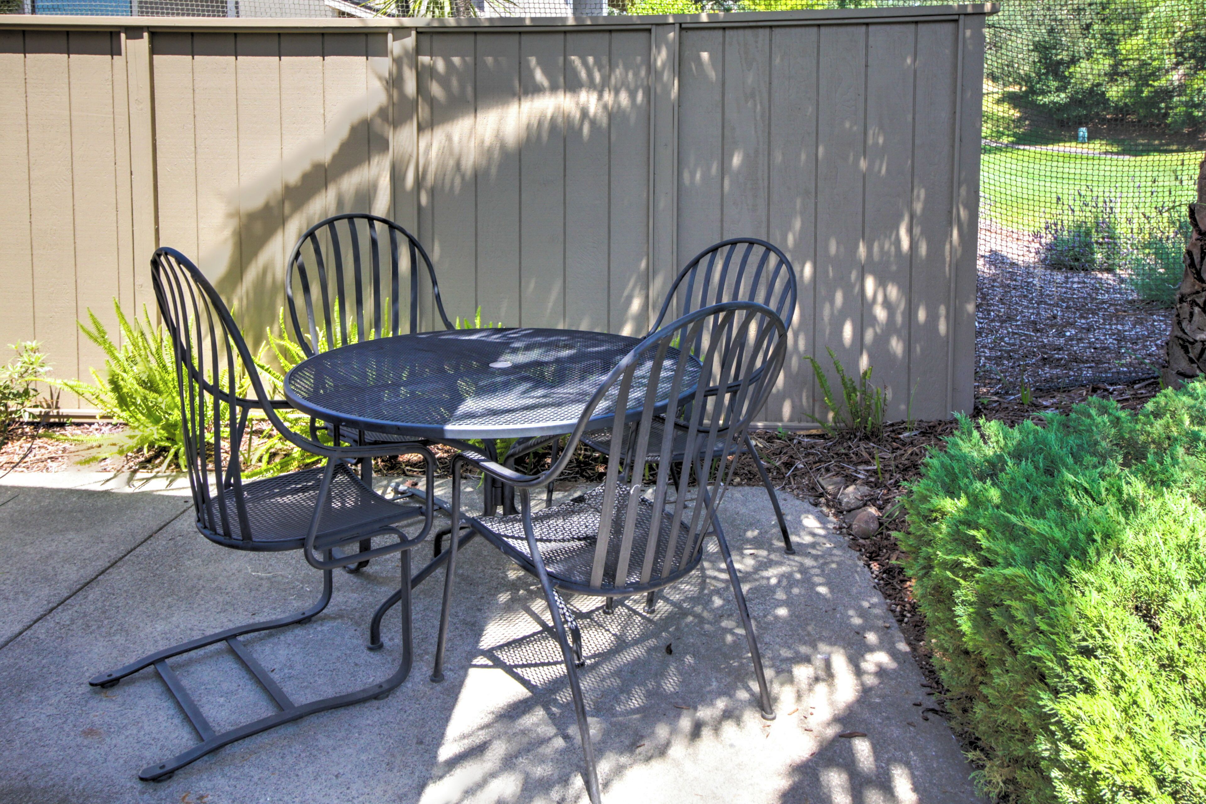 A patio with a metal table and chairs, a concrete floor, and a wooden fence.