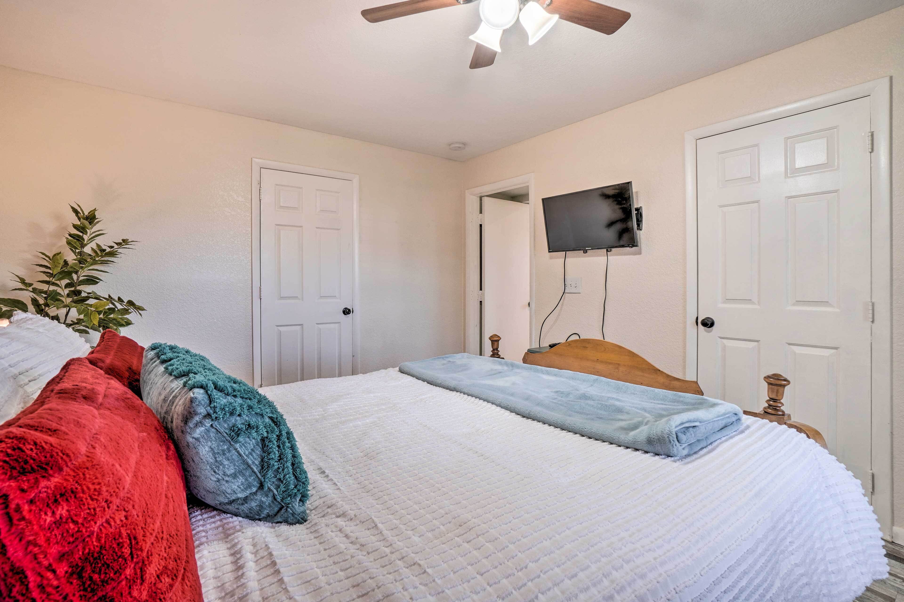 A bedroom with a bed, a ceiling fan, a television mounted on the wall, and a door.