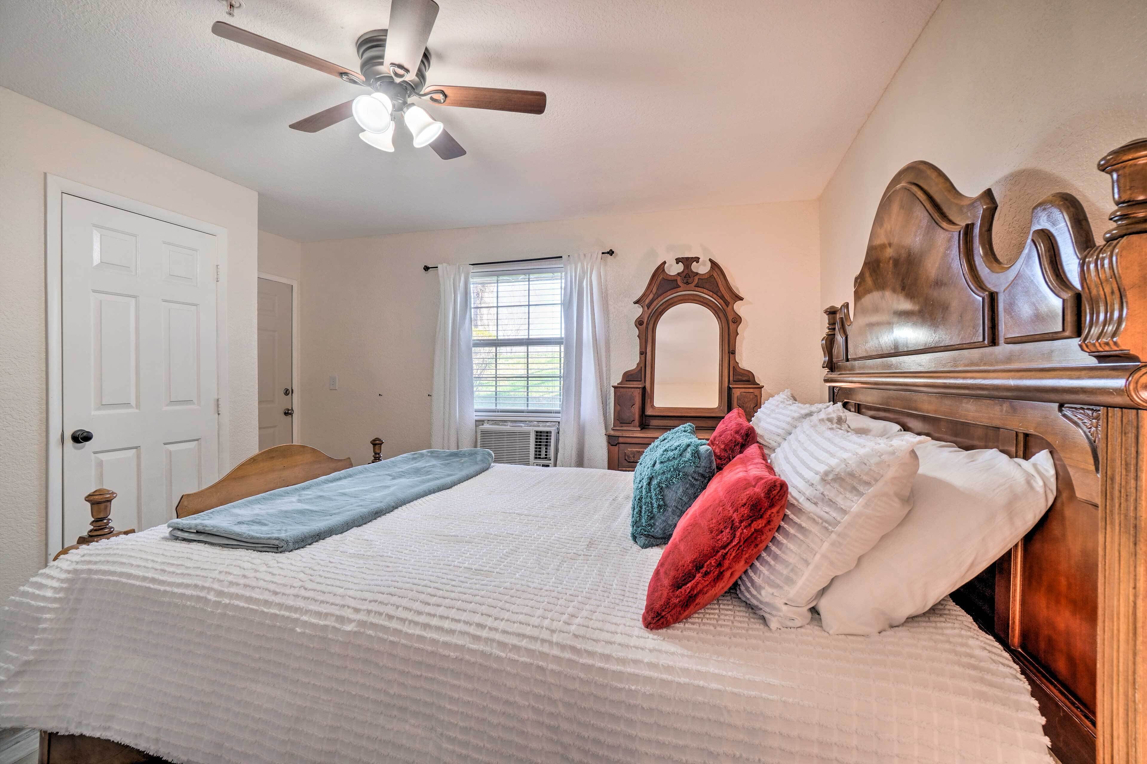 A bedroom with a wooden bed, a ceiling fan, a window with curtains, and a mirror.