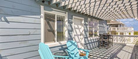 Une véranda abritée avec deux fauteuils Adirondack, une petite table et une vue sur une maison dotée d’un balcon.
