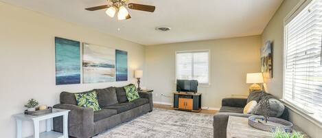 A living room with a ceiling fan, a gray sofa, a coffee table, a TV stand, and a window with blinds.