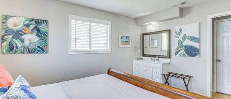 A bedroom with a bed, a ceiling fan, a window with blinds, a dresser, a mirror, and wall art.