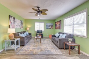 A living room with two grey sofas, a wooden coffee table, a small side table, a ceiling fan, and artwork on the walls.