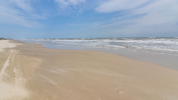 Een strand met een brede zandvlakte en rustige golven.