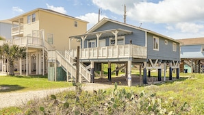 Een huis aan de kust met een balkon, een overdekte veranda en een trap naar de bovenverdieping.
