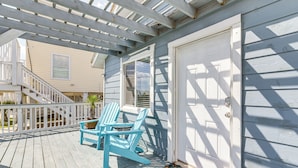 Een houten terras met twee blauwe Adirondack-stoelen, een witte deur en een trap naar een hoger gelegen niveau.
