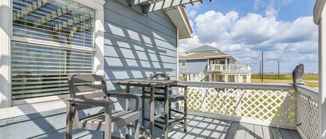 A wooden deck with a table and chairs, a white fence, and a view of a house in the background.